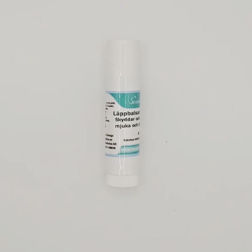 A white läppbalsam tube with a light blue label on a white background. The Swedish text highlights protection and softness, enriched with sheasmör and vegetabiliska oljor. Features Scandinavian Herbs and product name: Läppbalsam - för alla årstider.