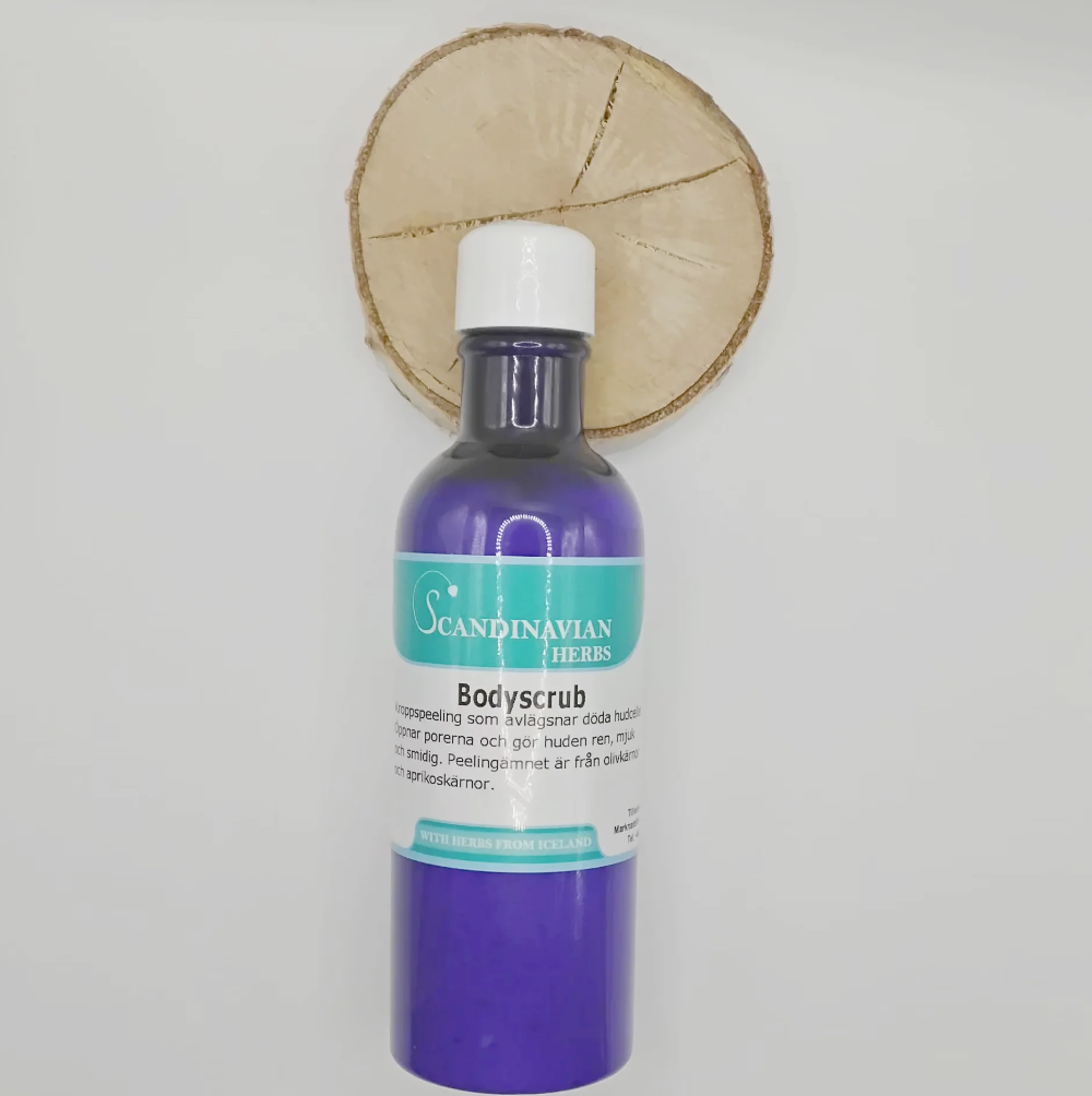A blue bottle of Bodyscrub by Scandinavian Herbs, containing olivkärnor, elegantly rests on a wooden slice. The white-capped bottle features a turquoise and white label, highlighting Icelandic herbs for a revitalizing experience.
