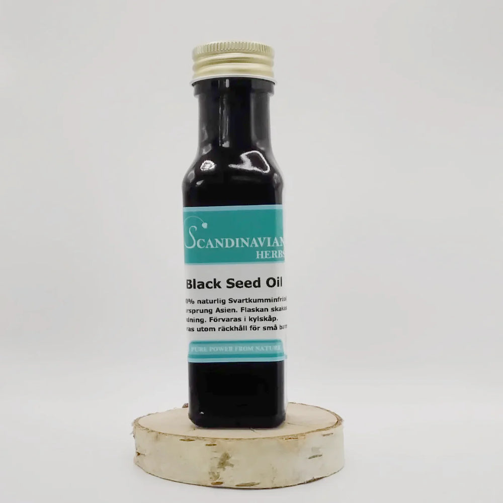 A Black Seed Oil - svartkumminolja bottle by Scandinavian Herbs is displayed on a round wooden platform. With its dark appearance and screw cap, the blue and white label stands out against the plain white background elegantly.
