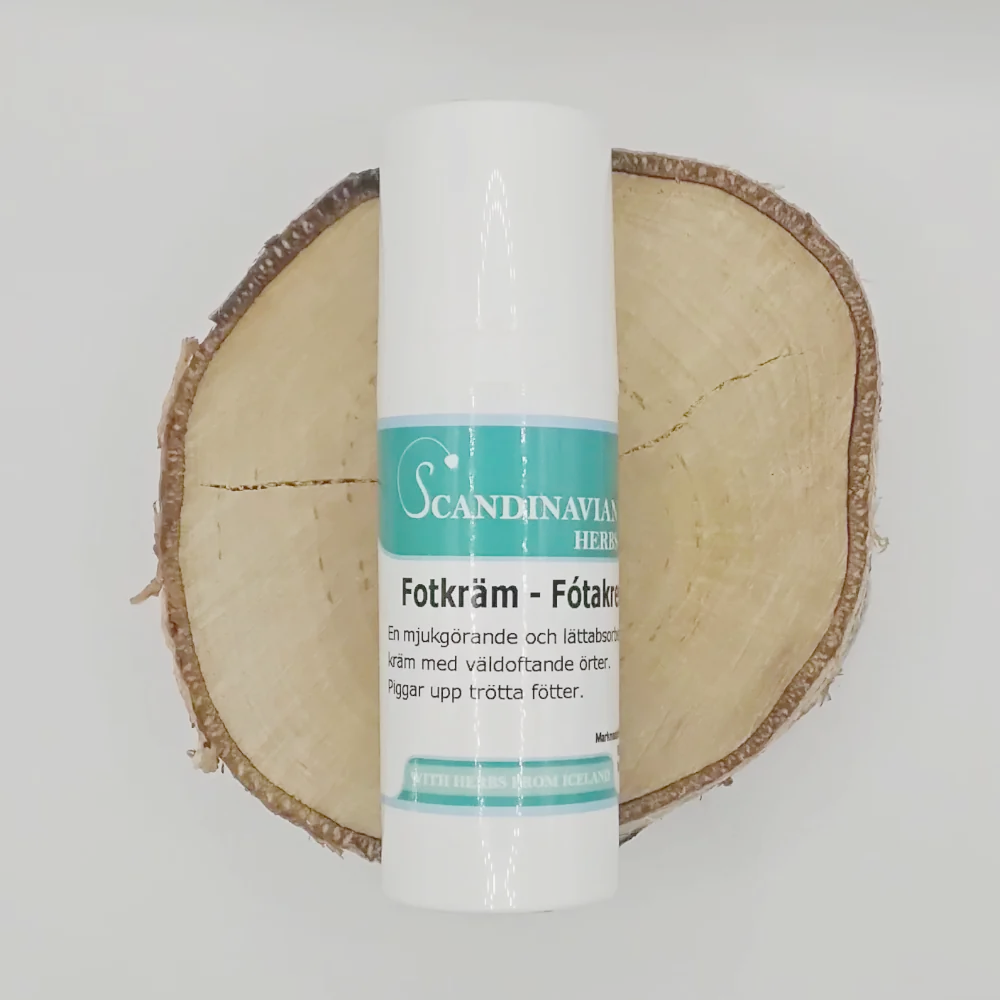 A white cylindrical bottle of Scandinavian Herbs Fotkräm, effektiv mot fotsvett och trötta fötter, stands on a tree trunk cross-section. Its light blue and white label in Swedish contrasts with the rustic charm of bark and wood grain in this sprucken hud remedy scene.