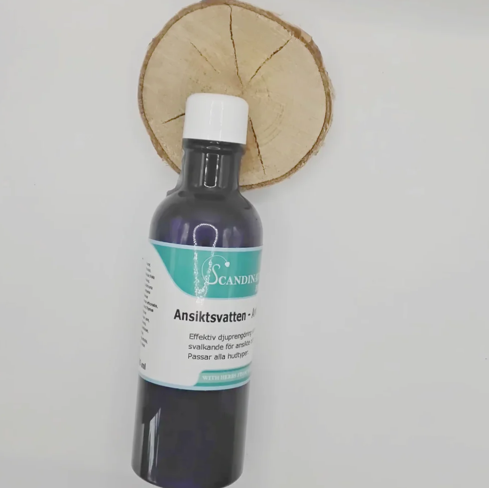 A bottle of black liquid labeled Ansiktsvatten -giftfri rengöring med örter from Scandinavian Herbs stands upright against a wooden slice. The turquoise and white label with text and logo suggests its herbal origins, sealed by a white cap that preserves the natural essence.