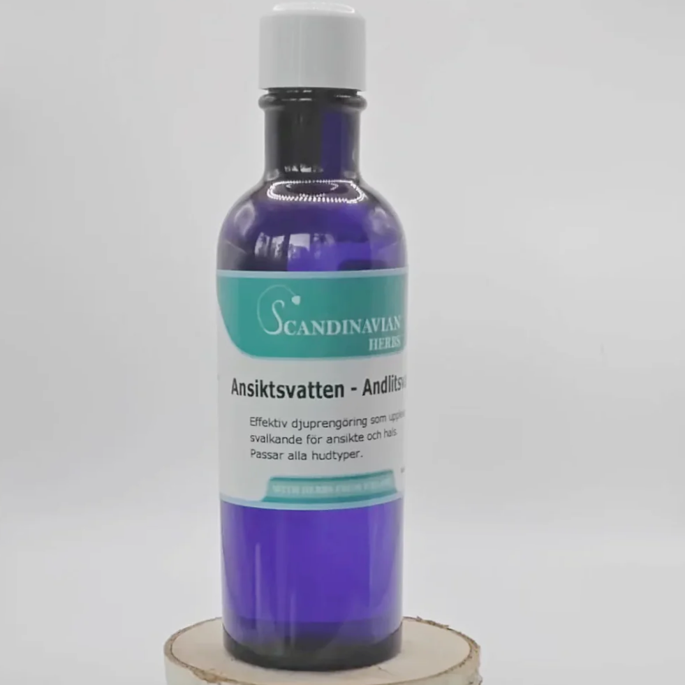 A blue glass bottle with a white cap, labeled Scandinavian Herbs Ansiktsvatten - giftfri rengöring med örter, is elegantly displayed on a light wooden circular stand against a plain white background.