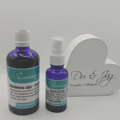 Two blue bottles from Scandinavian Herbs are placed beside a heart-shaped white box with Du & Jag and Två själar Ett hjärta. The larger bottle is labeled Kärleksolja, known for its afrodisiaka effekter, while the smaller is named Secret of Love, all part of the Kärlekspaket- en relationshöjare.