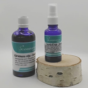 On a birch wood base, two blue glass bottles showcase Scandinavian design by Scandinavian Herbs. The left bottle, labeled Kärlekens olja, offers kärleksolja with afrodisiaka effekter, while the right, smaller bottle branded Secret of Love features a spray nozzle.