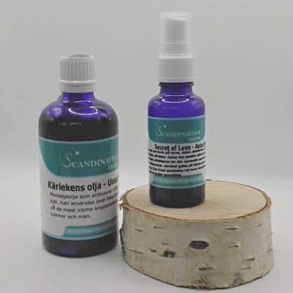 On a birch wood base, two blue glass bottles showcase Scandinavian design by Scandinavian Herbs. The left bottle, labeled Kärlekens olja, offers kärleksolja with afrodisiaka effekter, while the right, smaller bottle branded Secret of Love features a spray nozzle.