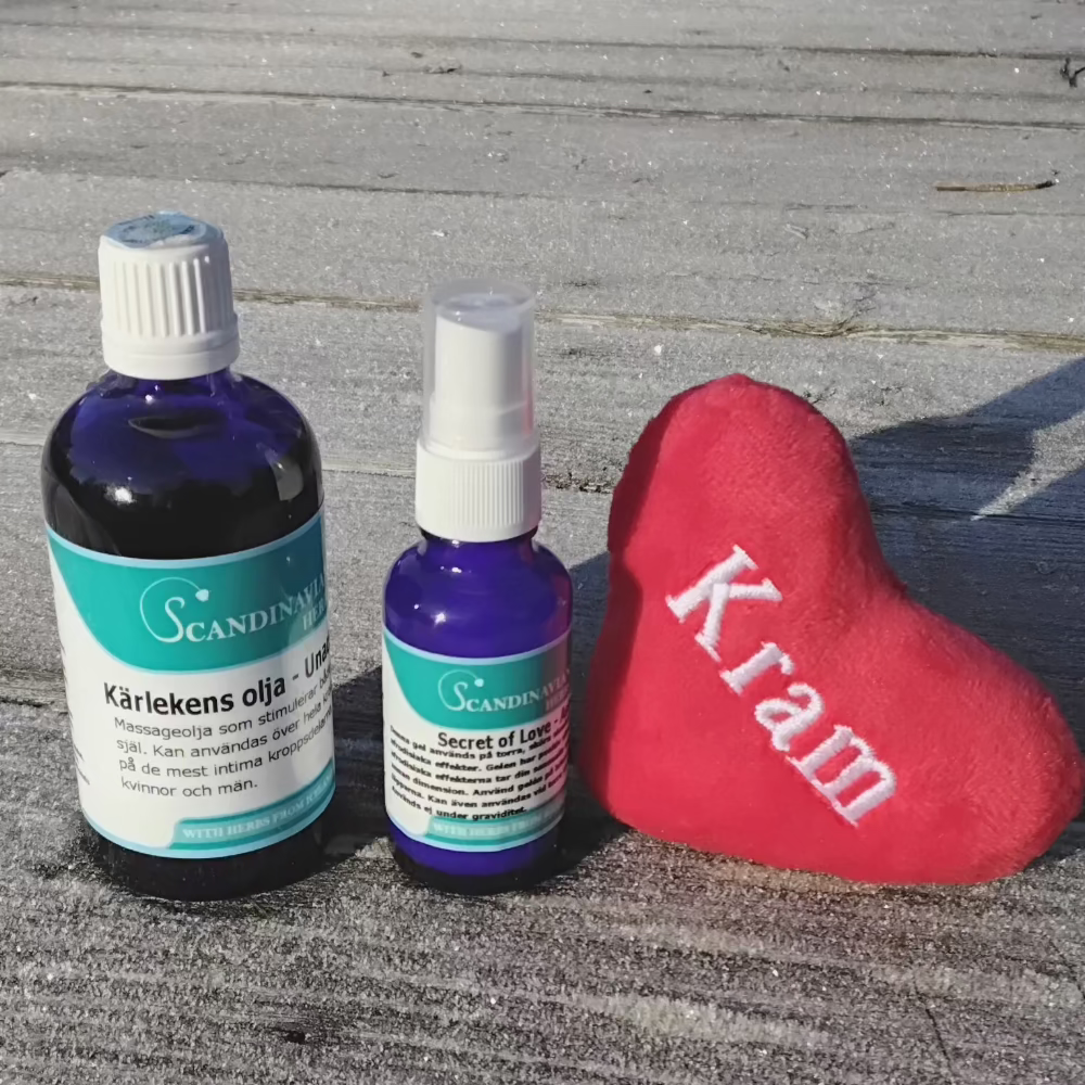 Two blue bottles with Swedish labels from Scandinavian Herbs Kärlekspaket- en relationshöjare sit on wood beside a plush red heart labeled Kram, bathed in sunlight, suggesting loves secret and afrodisiaka effekter through gentle shadows.